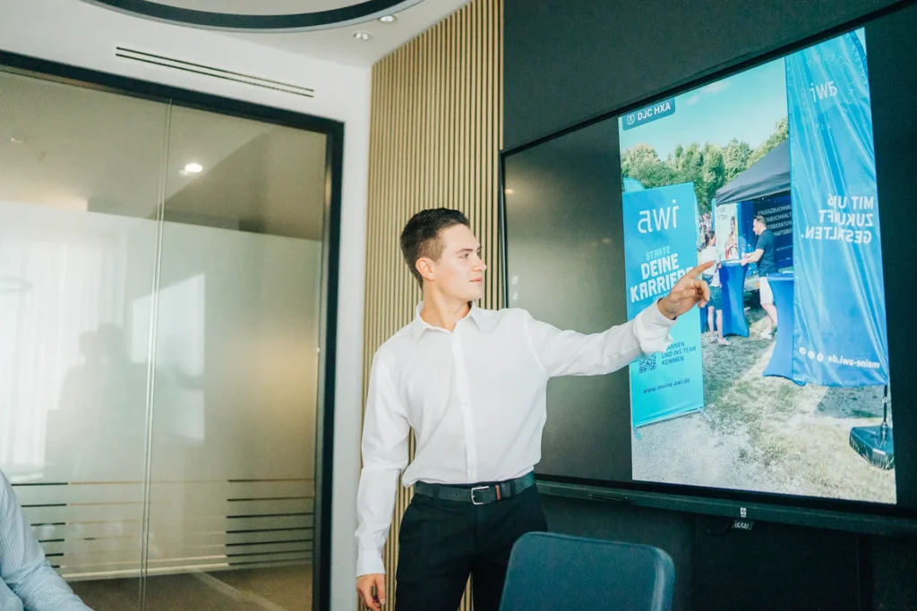 Junger Mann präsentiert eine Employer-Branding-Kampagne von awi mit Fokus auf Karrierestart und Arbeitgeberattraktivität auf einem digitalen Bildschirm.
