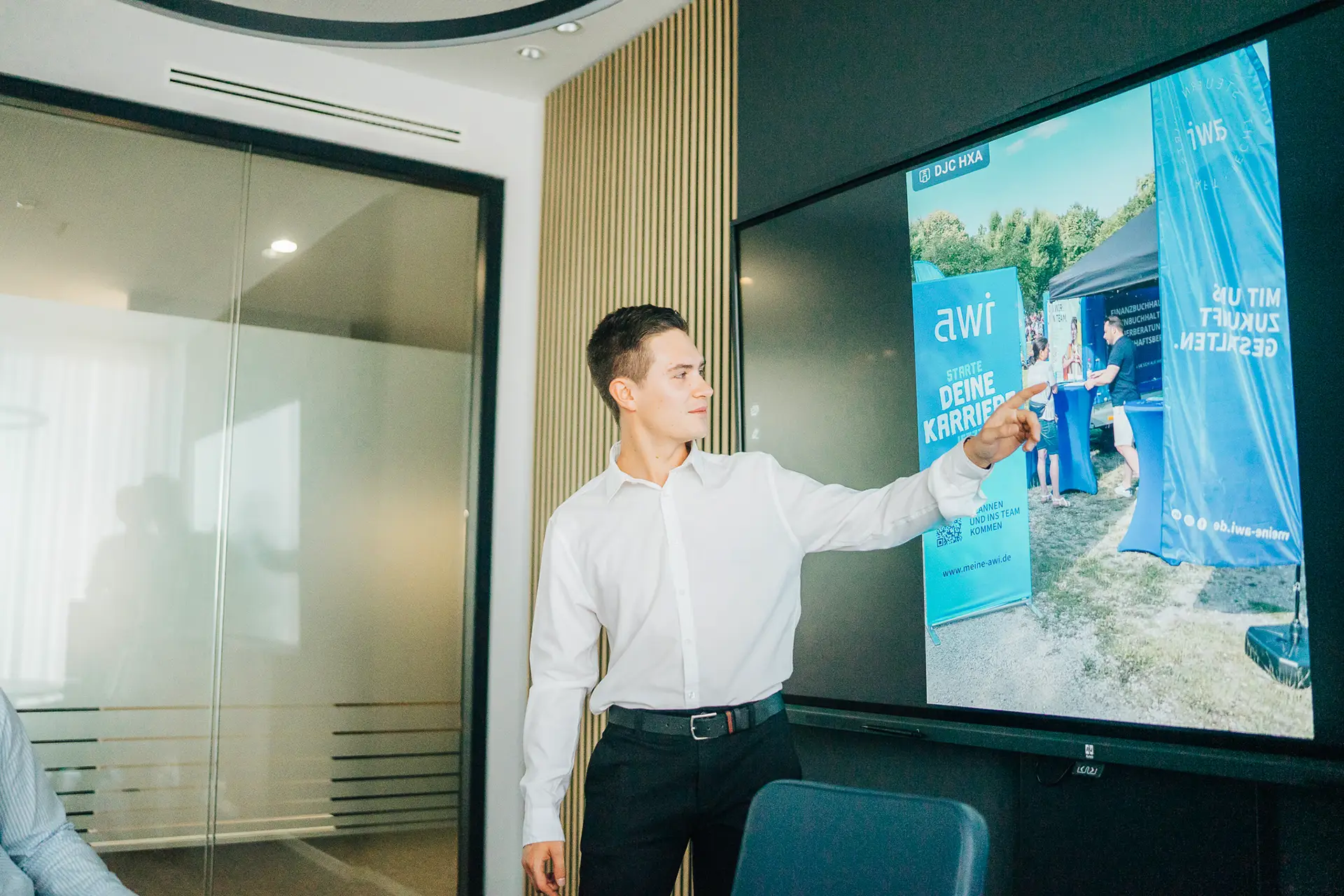 Junger Mann präsentiert eine Employer-Branding-Kampagne von awi mit Fokus auf Karrierestart und Arbeitgeberattraktivität auf einem digitalen Bildschirm.