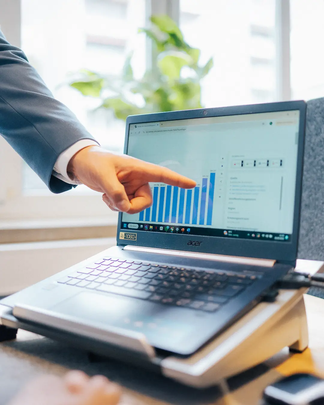 Unternehmensberatung in Augsburg: Ein Berater von awi consulting zeigt auf einen Laptop mit Datenanalyse und Balkendiagramm. Strategische Geschäftsberatung und Digitalisierung für Unternehmen in Augsburg.