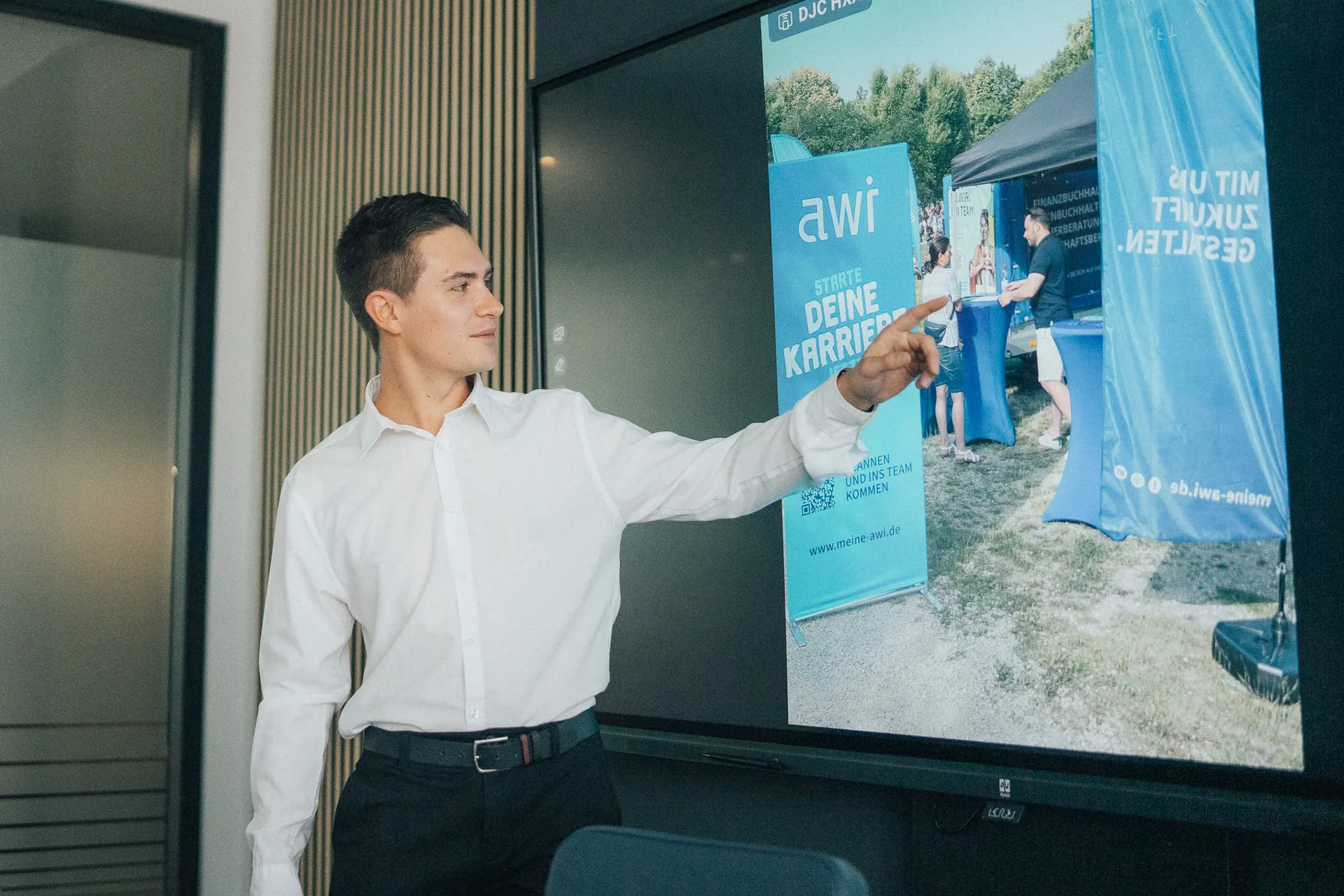 Junger Mann präsentiert eine Employer-Branding-Kampagne von AWI mit Fokus auf Karrierestart und Arbeitgeberattraktivität auf einem digitalen Bildschirm.