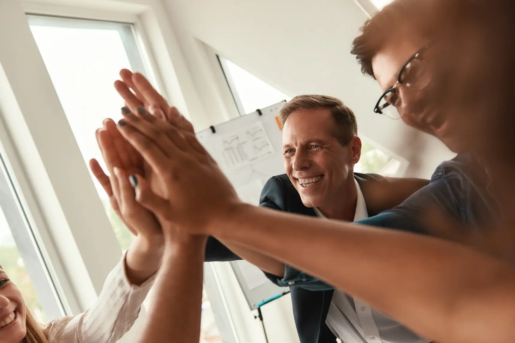 Team von Fachpartnern legt die Hände übereinander im Büro, Symbol für Zusammenarbeit und Partnerschaft rund um smarte Stromsteuerung und Stromintelligenz App.